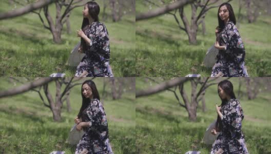 侧面的自信美丽的亚洲年轻女子身穿和服，坐在公园绿色的春天草地上，抚摸着长长的黑发。苗条美丽的女士享受阳光明媚的户外。休闲和女性气质。高清在线视频素材下载