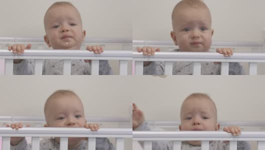 婴儿坐在婴儿床上，抓住婴儿床的栏杆，环顾四周高清在线视频素材下载