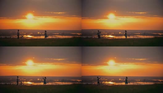 年轻的女子和她的丈夫在球场上打羽毛球，旁边站着他们的小儿子，日落夏夜高清在线视频素材下载