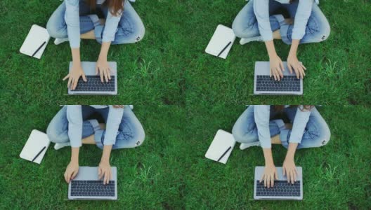 俯视图女人在笔记本键盘上打字，而工作在公园的绿色草地上高清在线视频素材下载