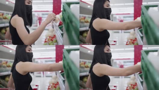 独立的亚洲妇女戴着口罩选择货架上的商品，站在超市货架前看零售超市内的产品，新冠肺炎大流行，选择食品高清在线视频素材下载