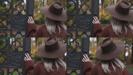 穿着棕色外套的时尚女孩在秋天公园附近的大门高清在线视频素材下载