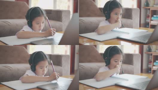 亚洲女童学生戴上耳机，通过视频电话与老师在线学习。由于Covid - 19大流行，在隔离期间，孩子正在用笔记本电脑在家学习。高清在线视频素材下载