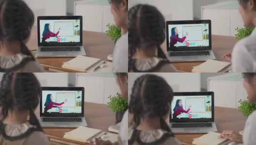 由于冠状病毒大流行，亚洲小女孩通过数字远程互联网会议从学校老师那里学习在线课程。孩子看电脑笔记本电脑屏幕与母亲的协助。高清在线视频素材下载