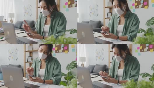 年轻的亚洲女性戴着医用口罩与忙碌的企业家在起居室远距离工作。高清在线视频素材下载