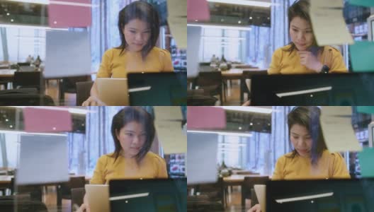 具有吸引力的自由职业亚洲女性创意人士，穿着休闲的黄色布手点和书写纸笔记贴提醒在共同工作空间的新生活方式与思考和新鲜的情感高清在线视频素材下载