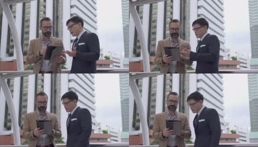两个商务人士白种人与亚洲人同事伙伴关系讨论商业项目计划与使用数字平板电脑在城市。商务会议、技术、并购概念。高清在线视频素材下载