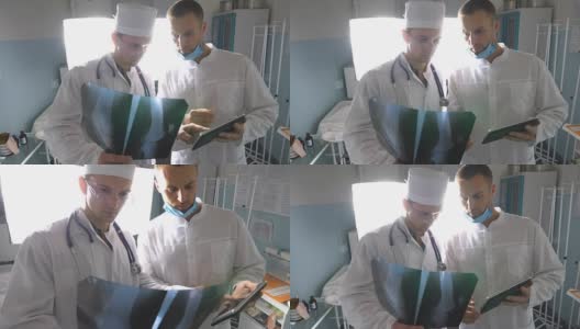 男医生一边使用平板电脑一边互相咨询病人的x光片。医院的医务人员检查x光照片。两位白种人医生观看核磁共振图像并讨论它。前视图高清在线视频素材下载
