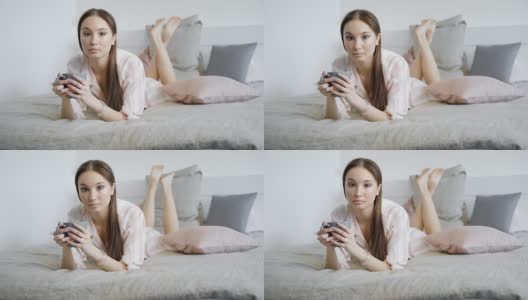 一个年轻漂亮的女士在床上喝热饮的肖像，女士拿着一个杯子，穿着睡衣高清在线视频素材下载