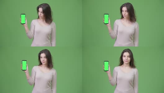 年轻美丽的女人在绿色背景下展示手机高清在线视频素材下载