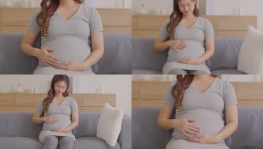 快乐的孕妇坐在沙发上，抱着抚摸着自己的大肚子。怀孕的年轻女子在家里享受着未来的生活。母亲怀孕的概念。软的焦点。多莉出去拍摄高清在线视频素材下载