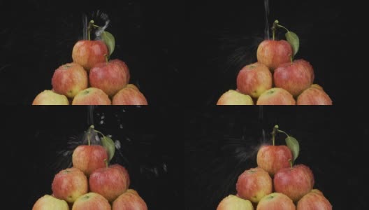 一股水流落在一堆苹果上。落下的水，飞溅和水滴在黑色的背景上。孤立的高清在线视频素材下载