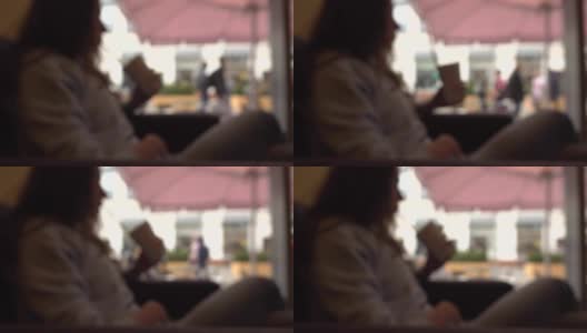 模糊的黑发女孩有她的饮料与吸管在一个咖啡馆靠窗。慢动作背景散景拍摄高清在线视频素材下载