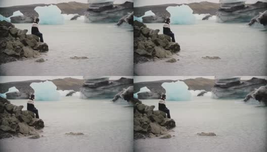 年轻英俊的男子坐在冰礁湖的岩石上欣赏风景。独自探索冰岛的男性高清在线视频素材下载