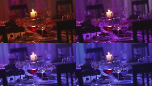 餐厅的宴会桌上放着玻璃杯和一支蜡烛，宴会桌上放着一杯红白葡萄酒，背景上放着一支燃烧的蜡烛，桌子上挂着一支装饰性的蜡烛高清在线视频素材下载