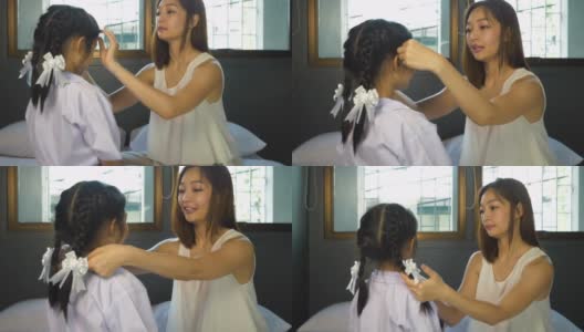 亚洲母亲在她的卧室里穿着校服给女儿做头发，准备早上上学。高清在线视频素材下载