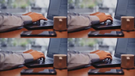 使用笔记本电脑工作的商务人士。穿蓝色衬衫在键盘上打字的人。一个人在笔记本电脑上工作的特写。一个人在办公桌上的特写，笔记本电脑，咖啡杯和智能手机。高清在线视频素材下载