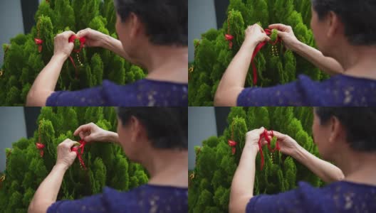 亚洲华人微笑女性活跃的老年人在树上装饰中国新年装饰品高清在线视频素材下载