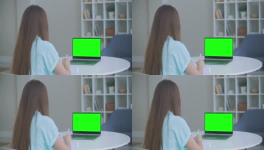 女孩在笔记本电脑上做笔记绿色模拟屏幕。女孩在网上学习电脑高清在线视频素材下载