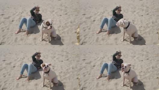 一个可爱的白人女人和她的白色拳击狗在沙滩上放松的慢动作高清在线视频素材下载