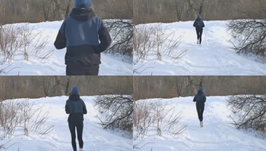 后视图跑步年轻的女孩穿着深色运动服慢跑在公园的树与雪的背景。健康的生活方式的概念。高清在线视频素材下载
