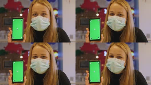 咖啡馆里，一名戴着医用口罩的女子拿着一部带有色度键的手机。高清在线视频素材下载
