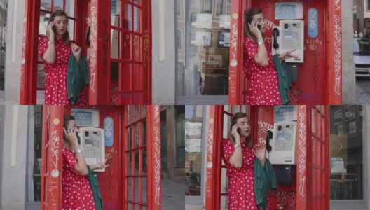 一个年轻女子站在一个旧的红色电话亭里用手机聊天高清在线视频素材下载