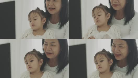 一位泰国母亲带着她的宝贝女儿在她的房间里用笔记本电脑看卡通片高清在线视频素材下载