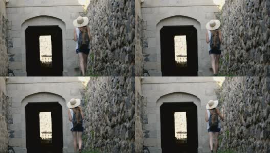 一个戴着帽子的年轻女子沿着古老的城墙走着，抚摸着她高清在线视频素材下载