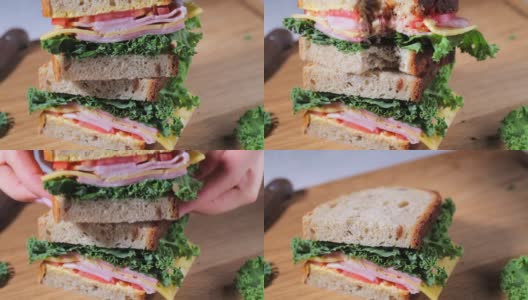 夹着火腿、奶酪、蔬菜和羽衣甘蓝在木板上吃三明治。高清在线视频素材下载