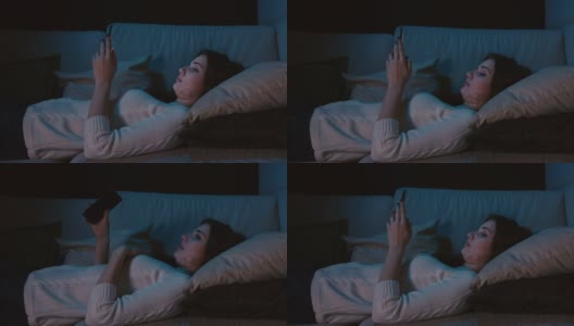 千禧一代女性躺在床上拿着手机，在在线约会应用上刷照片，在社交网络上输入信息。智能手机成瘾高清在线视频素材下载
