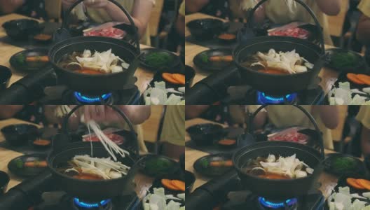 这名女子在一家日本餐馆里把金蘑菇放进涮锅里。和家人共进晚餐。高清在线视频素材下载