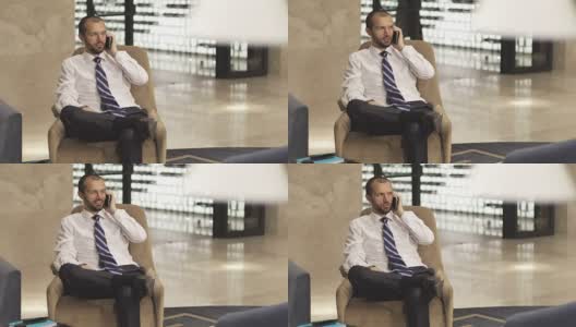 一位时尚的商人坐在酒店大堂或办公室里使用手机。高清在线视频素材下载