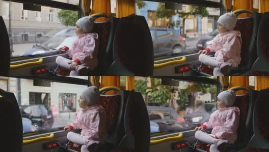 穿着粉红色夹克的金发小女孩，孩子坐在巴士车厢里。坐在她的座位上，透过玻璃窗看。高清在线视频素材下载
