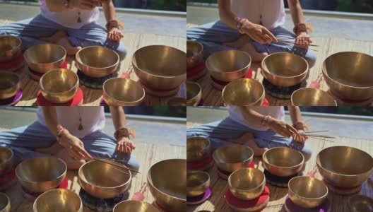 一名亚洲神药女大师表演藏式碗疗愈仪式的超慢镜头。用西藏唱碗冥想。她坐在凉亭里冥想，背景是美丽的瀑布高清在线视频素材下载