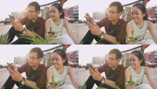 美丽的亚洲年轻人坐在购物车附近的地上，产品装满了食物，看着男人的手机上的照片高清在线视频素材下载