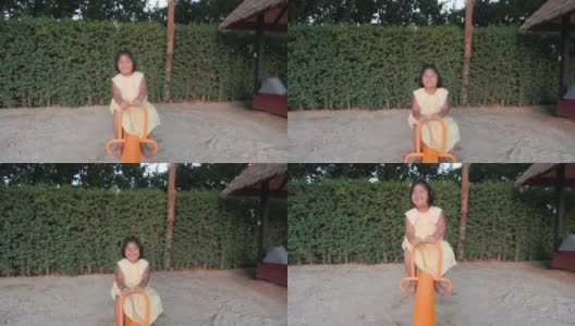 4K慢镜头:亚洲可爱女孩快乐地在公共操场玩跷跷板。高清在线视频素材下载