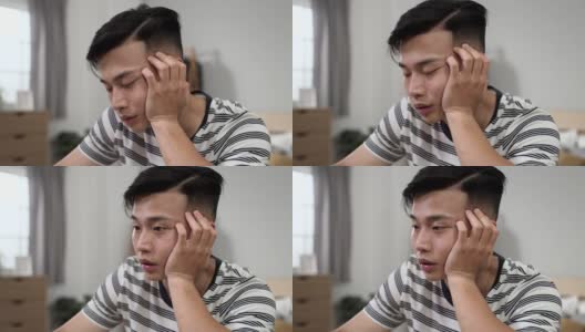 一个疲惫的中国年轻人抱着脸，努力不睡着，同时在他的卧室在互联网上学习封锁期间。高清在线视频素材下载