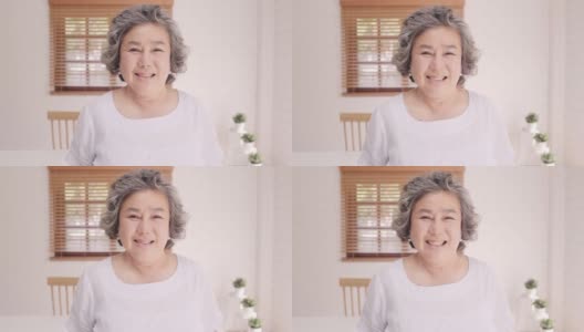 亚洲老年妇女感到幸福的微笑和看着镜头，而放松在客厅的沙发在家里。生活方式高级女性在家的概念。高清在线视频素材下载