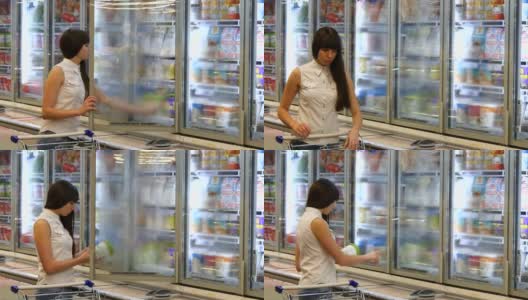 年轻女子推着购物车在超市的冷藏区打开玻璃门购买乳制品或冷藏食品。一个女孩走到商店的冰箱前，从里面拿东西高清在线视频素材下载