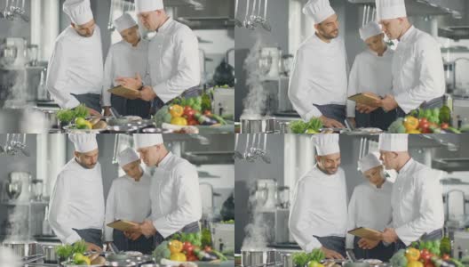 在现代厨房团队中，厨师们用平板电脑制作食谱，他们微笑着讨论。厨房里有很多食材，蔬菜，肉，汤。高清在线视频素材下载