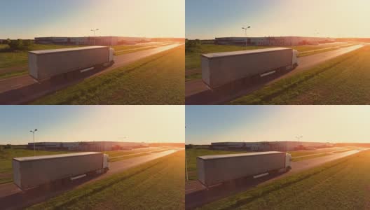在高速公路上移动的白色半挂车的鸟瞰图。在背景中可以看到仓库和工业装载建筑。日落。高清在线视频素材下载