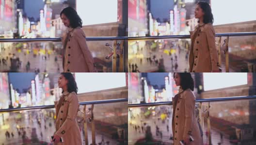 侧面的一个漂亮的快乐年轻的亚洲女人走在城市的街道在晚上与手机在手摇慢动作高清在线视频素材下载