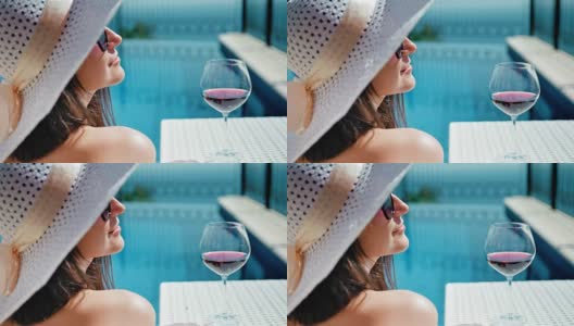 肖像微笑的漂亮女人在松软的帽子和太阳镜享受日光浴与酒杯的葡萄酒高清在线视频素材下载