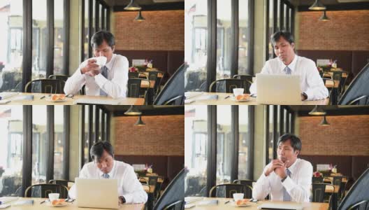 亚洲商人喝咖啡，注入活力，开始在商务办公室用笔记本电脑工作。沮丧压力大的中年危机商人的概念。高清在线视频素材下载