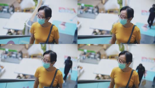 戴着医用口罩站在购物中心自动扶梯上的亚洲老人。高清在线视频素材下载