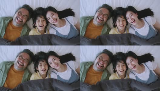 幸福亚洲可爱的一家人一起躺在床上，笑亚洲父母和儿子在毯子下看着摄像机俯视图家的家庭概念高清在线视频素材下载
