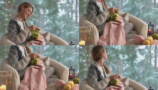 年轻女子在客厅里织着温暖的羊毛衫，窗外是雪景高清在线视频素材下载