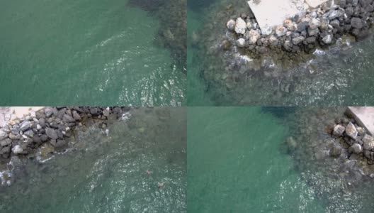 在希腊阿基亚帕拉斯凯维哈尔基迪基地区，鸟瞰夏天美丽的绿松石海，码头和岩石上冒出的水，无人机向上和侧移动高清在线视频素材下载