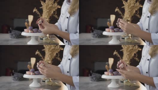 近距离拍摄的女人用奶油将两半的蛋白杏仁饼干连接起来。围裙上的铭文，模特的名字叫尼娜·洛斯高清在线视频素材下载